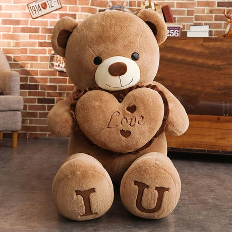 Brown teddy bear with a heart that says 'Love' and letters 'I' and 'U' on a wooden floor.
