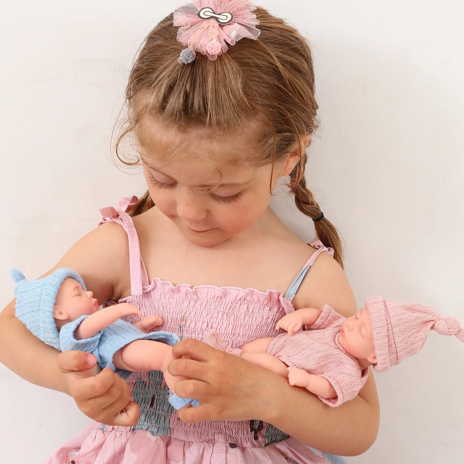 A Young girl holding two dolls, one blue and one pink.