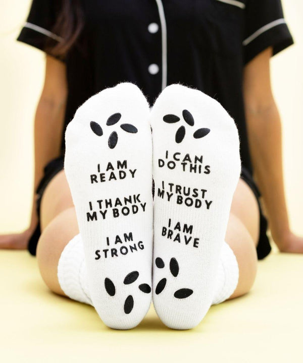 White birthing affirmation hospital socks with motivational text for labor and delivery comfort.