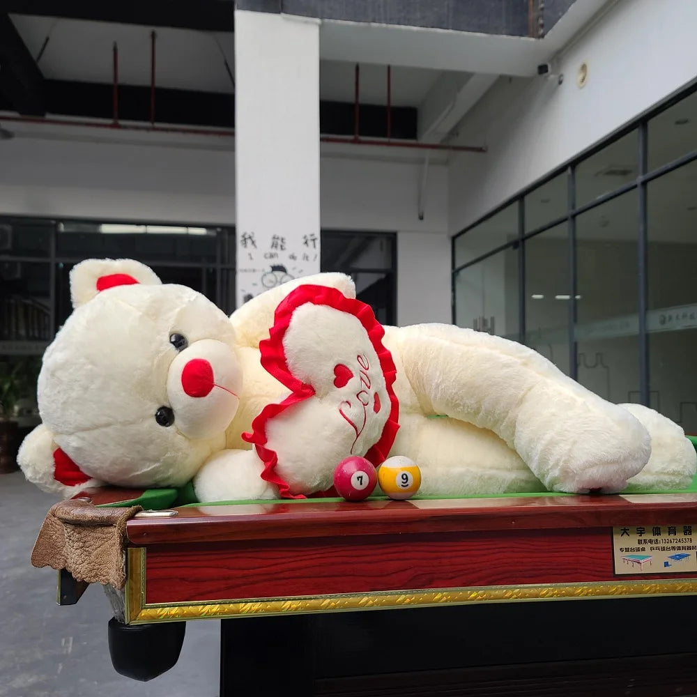 Two white teddy bear plush toys with red hearts styled on a pool table for gift display.