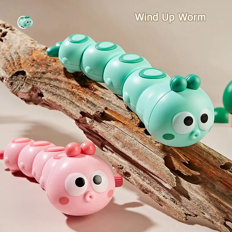 Mint green and pink wind-up caterpillar toys on a piece of driftwood