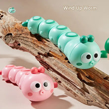 Mint green and pink wind-up caterpillar toys on a piece of driftwood