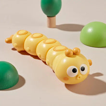 Yellow wind-up caterpillar toy with big eyes on a beige background
