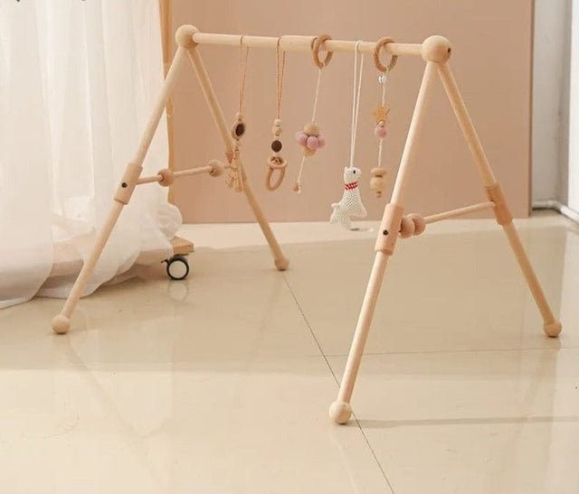 Wooden baby play gym with hanging toys on a light wooden floor.
