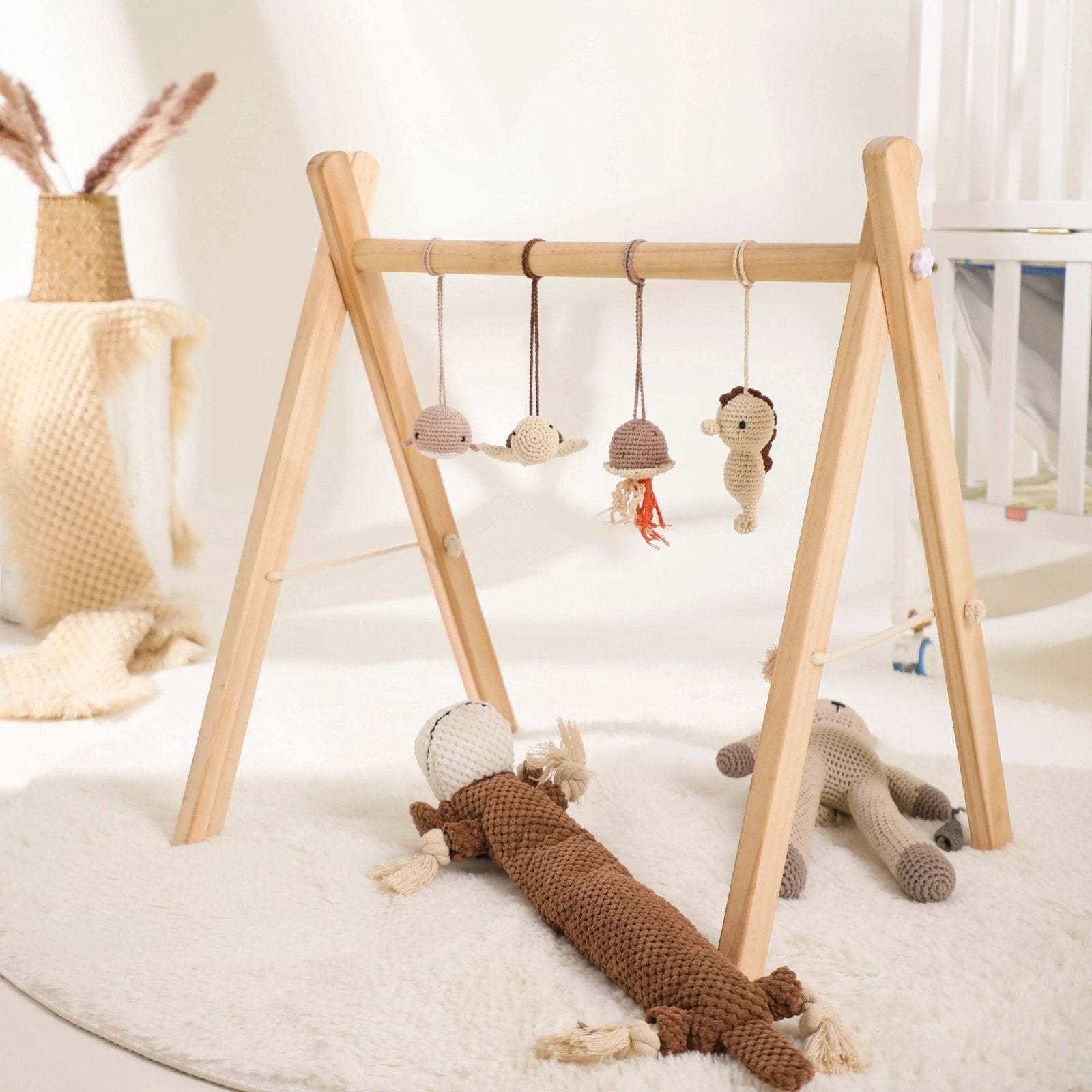 Wooden baby play gym with hanging toys set up in a nursery, encouraging reaching and grasping during tummy time.