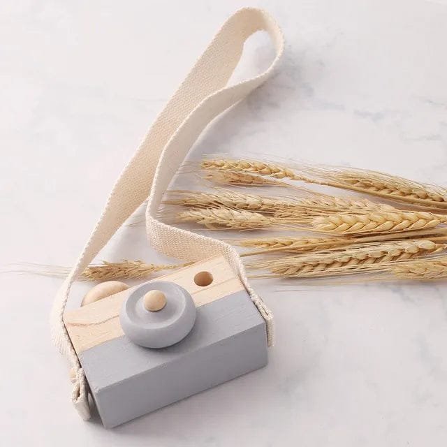 Wooden camera pendant with strap styled beside dried wheat, a handmade Montessori toy for nursery decor and play.